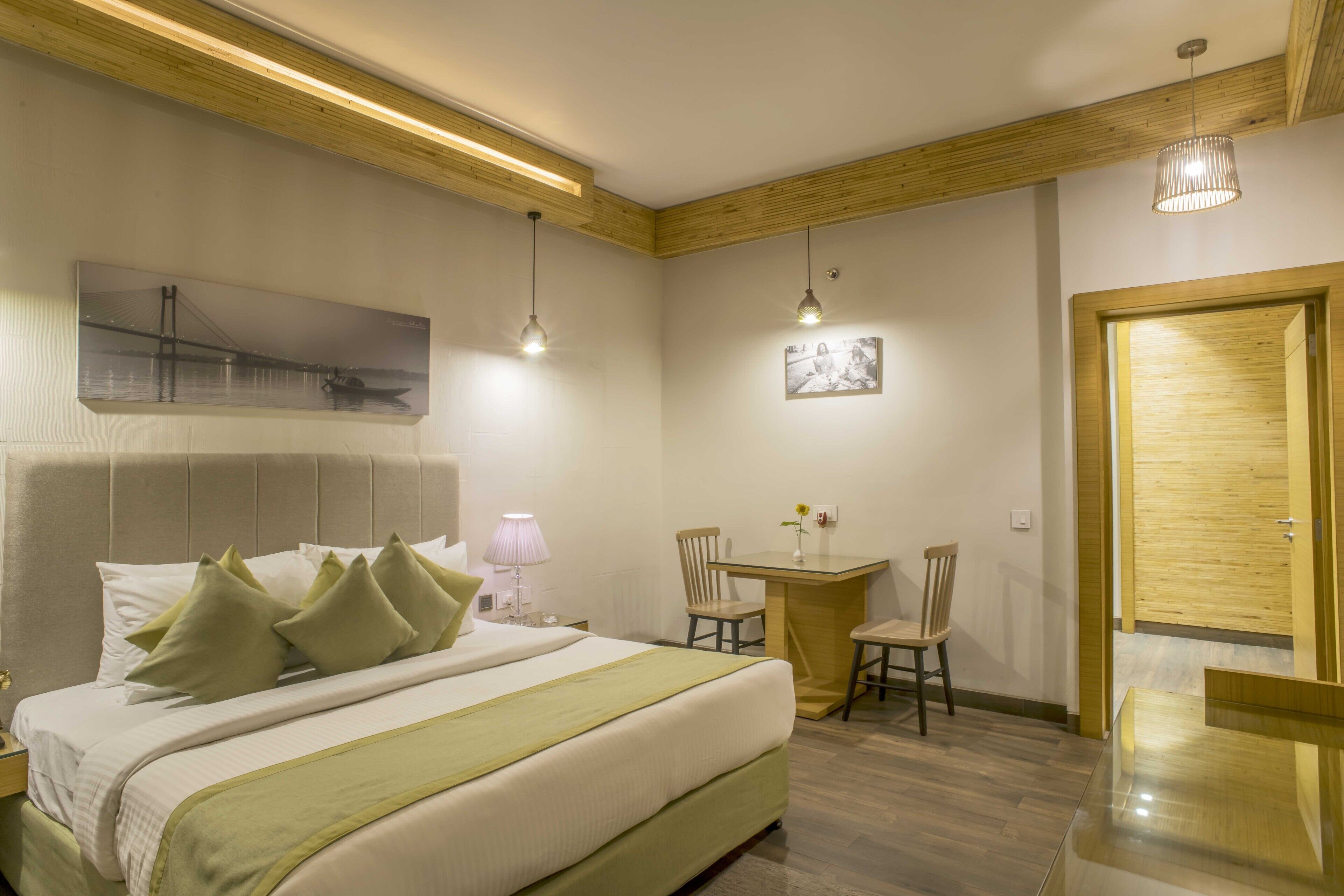 Habitación de hotel con una cama grande, una mesita, dos sillas, una puerta de madera y un techo con vigas de madera.