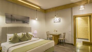 Habitación de hotel con una cama grande, una mesita, dos sillas, una puerta de madera y un techo con vigas de madera.