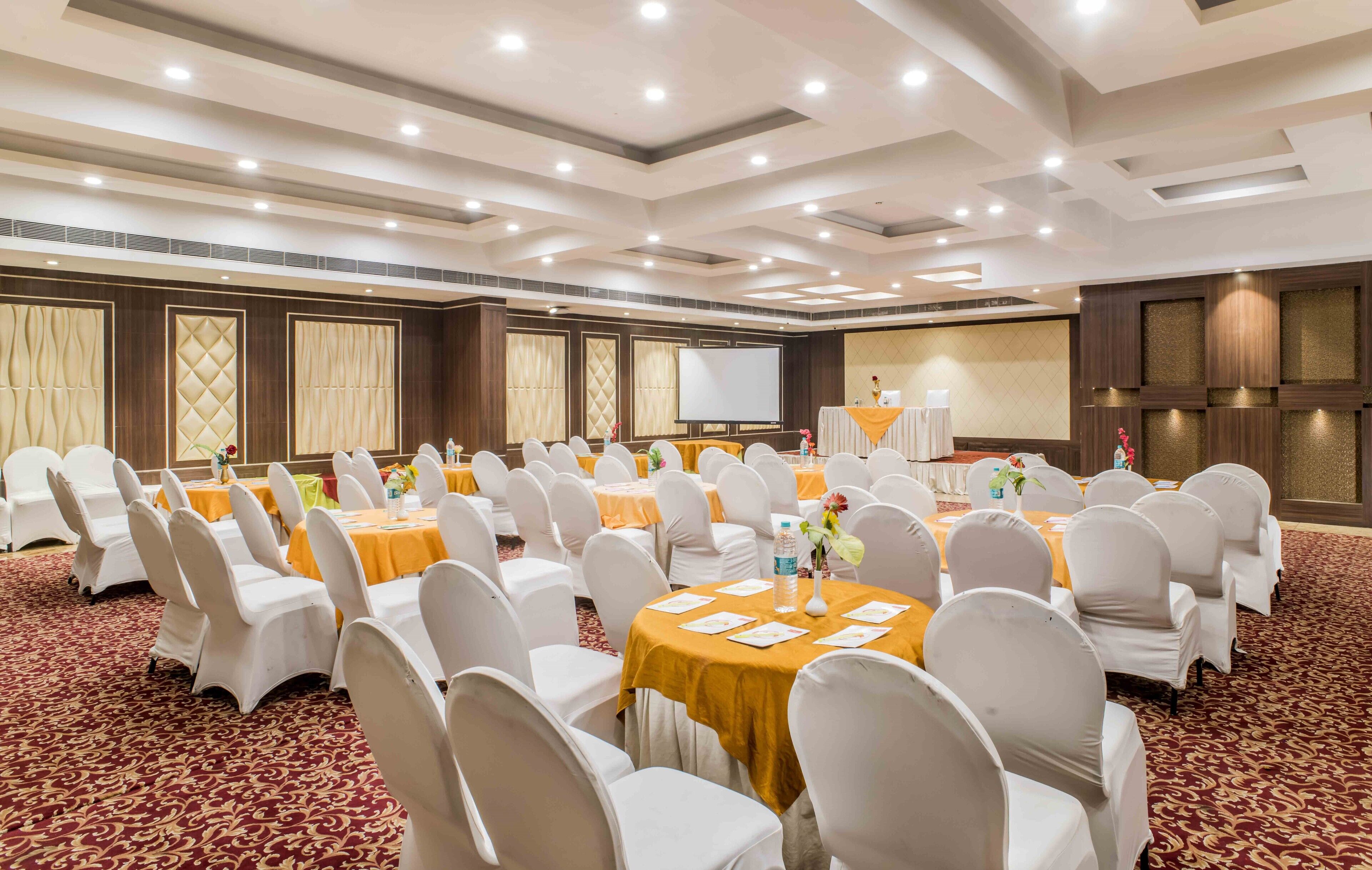 A conference room with round tables, white chairs, and a projector screen.