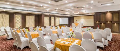 A conference room with round tables, white chairs, and a projector screen.