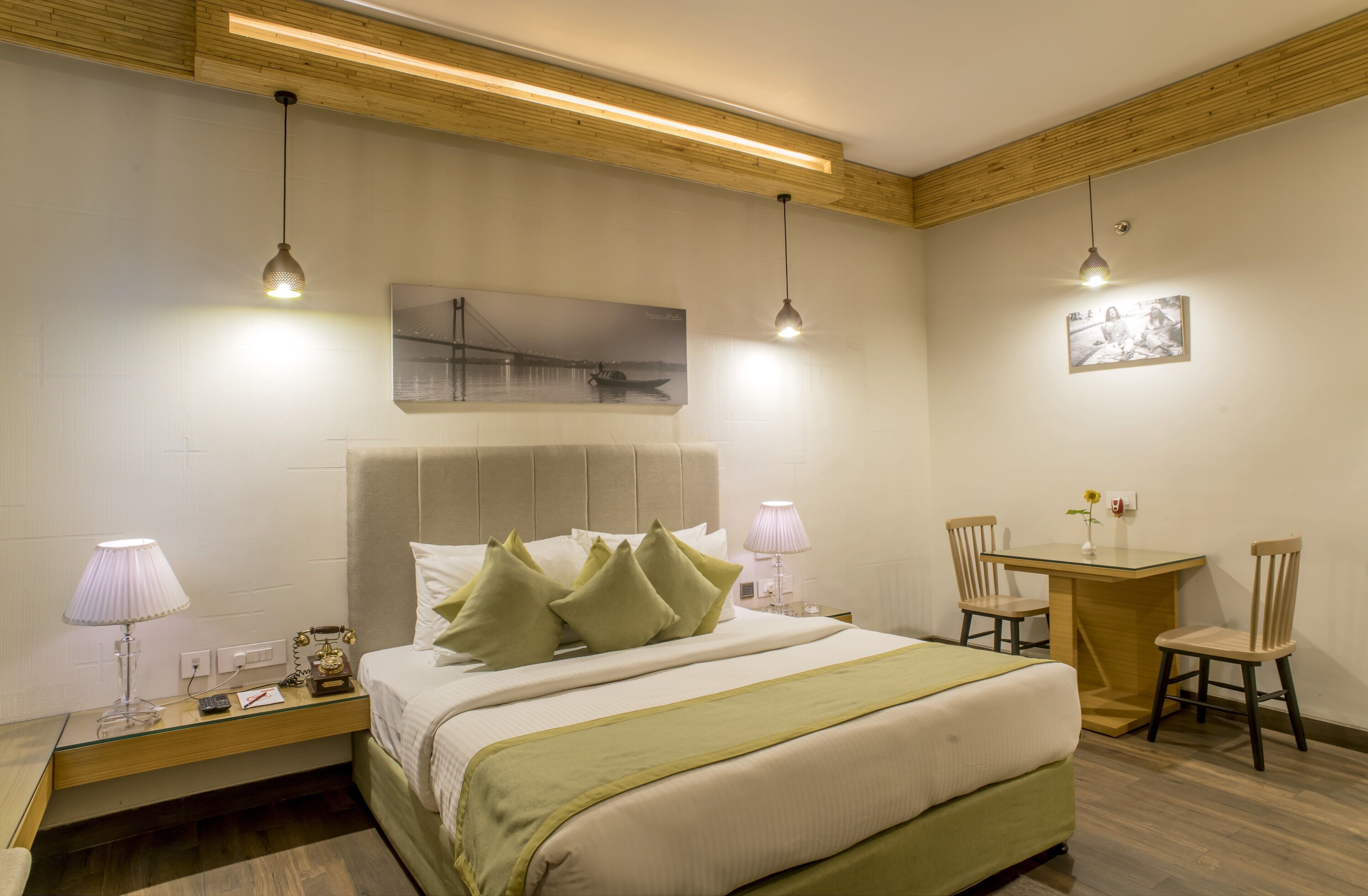 A hotel room with a bed, bedside lamps, a desk with two chairs, and a framed picture on the wall.