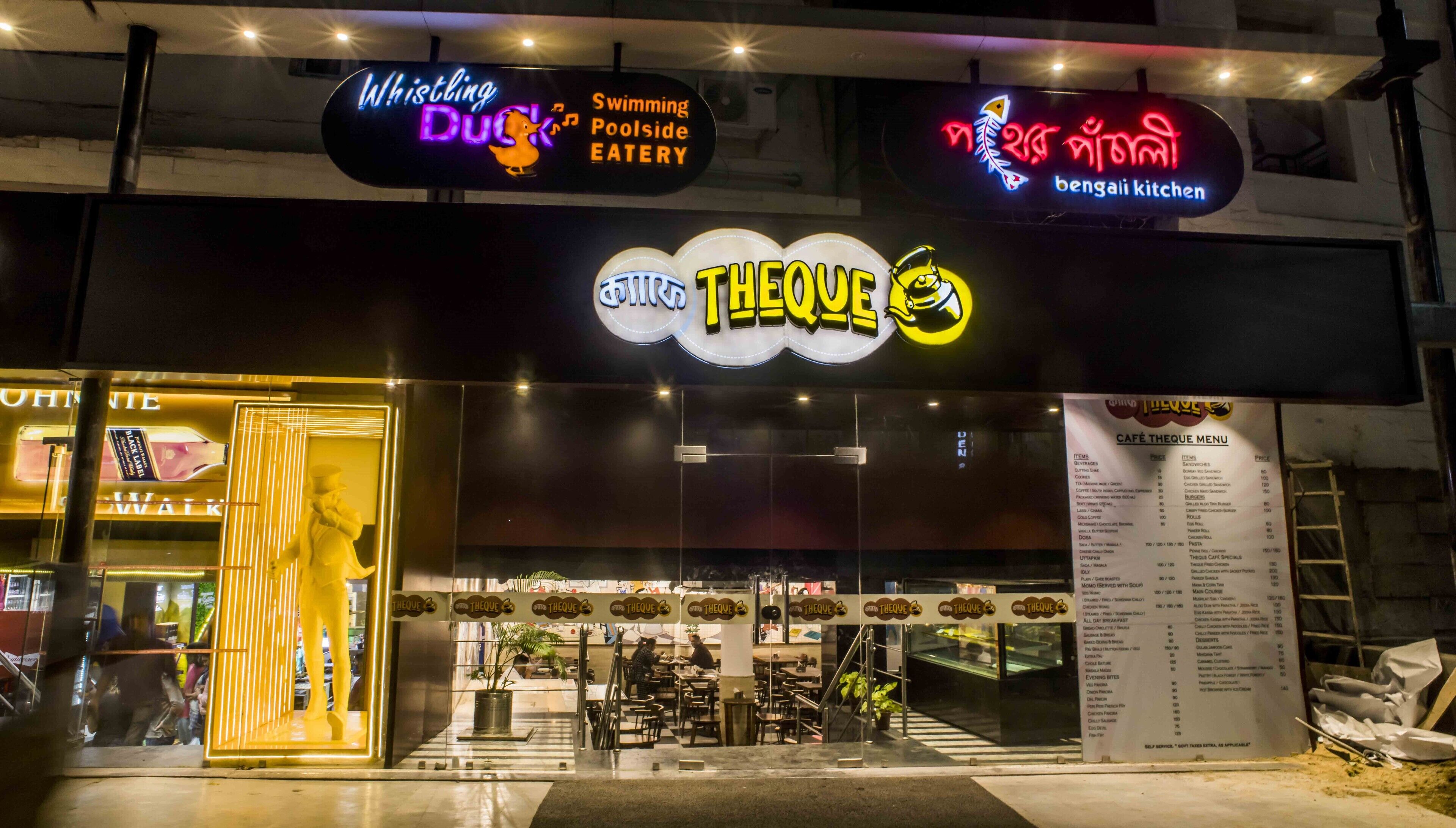 Un restaurante llamado 'Theque' con letreros de neón, una pizarra de menú y mesas al aire libre.