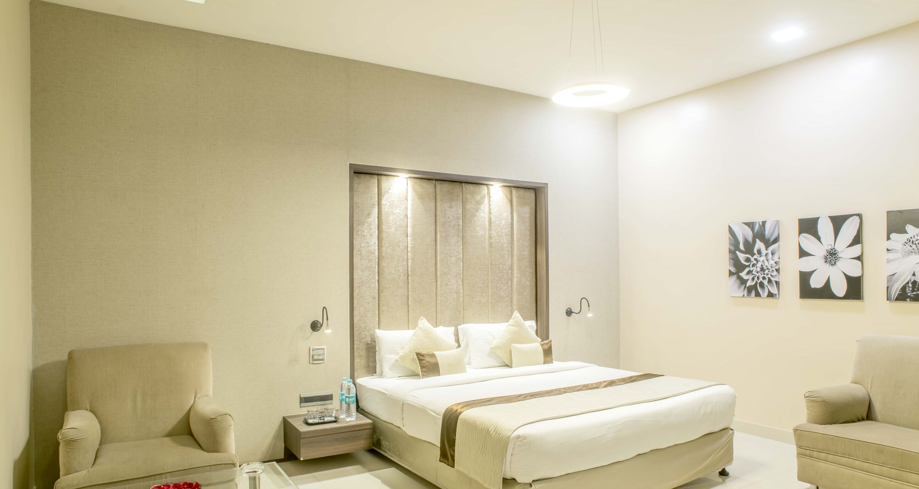 Une chambre d’hôtel avec un grand lit, une table de chevet avec une lampe, une chaise et des œuvres d’art accrochées au mur.