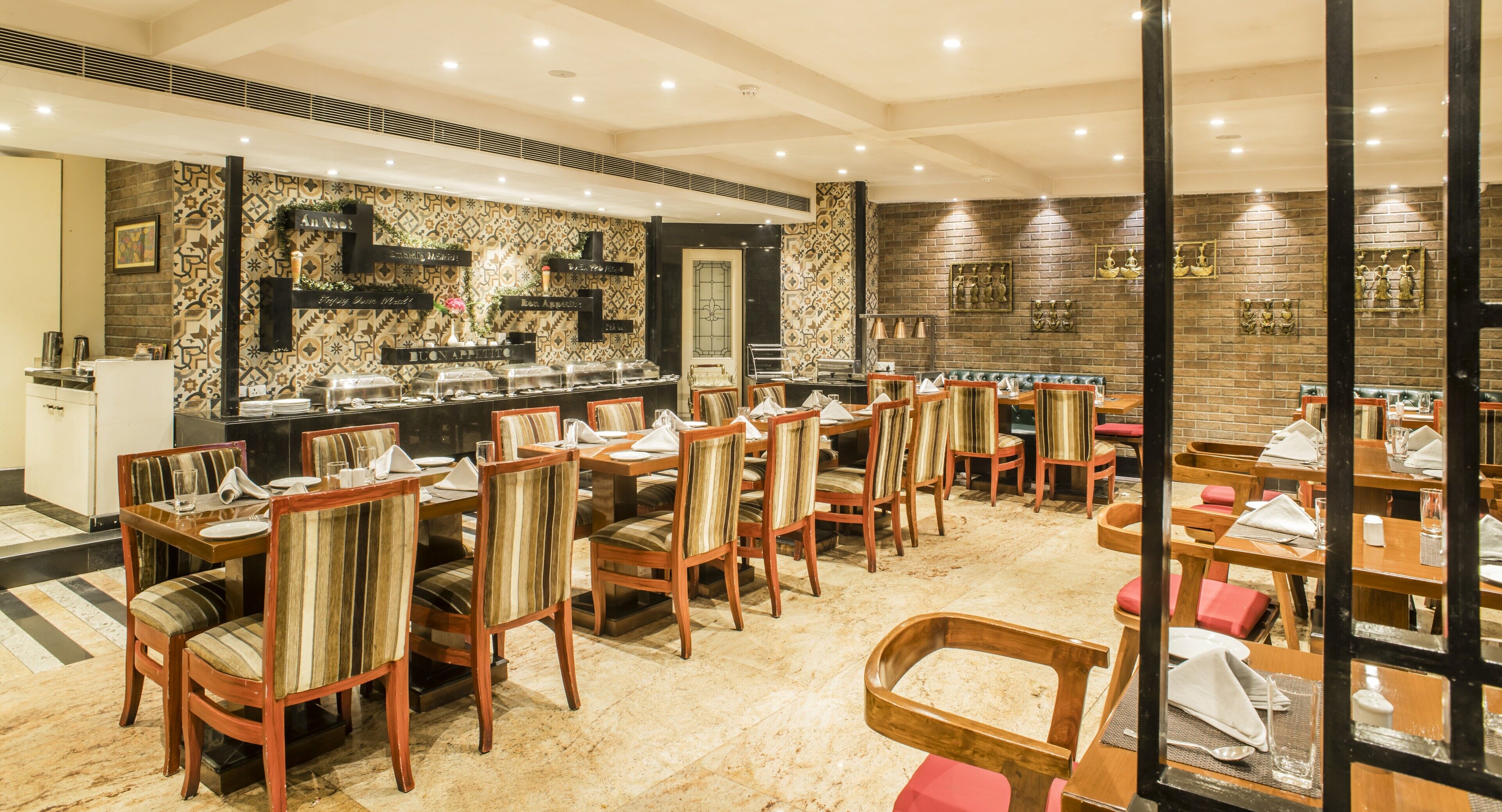 A restaurant with multiple tables and chairs, a buffet area, and a decorative wall with patterned tiles and artwork.