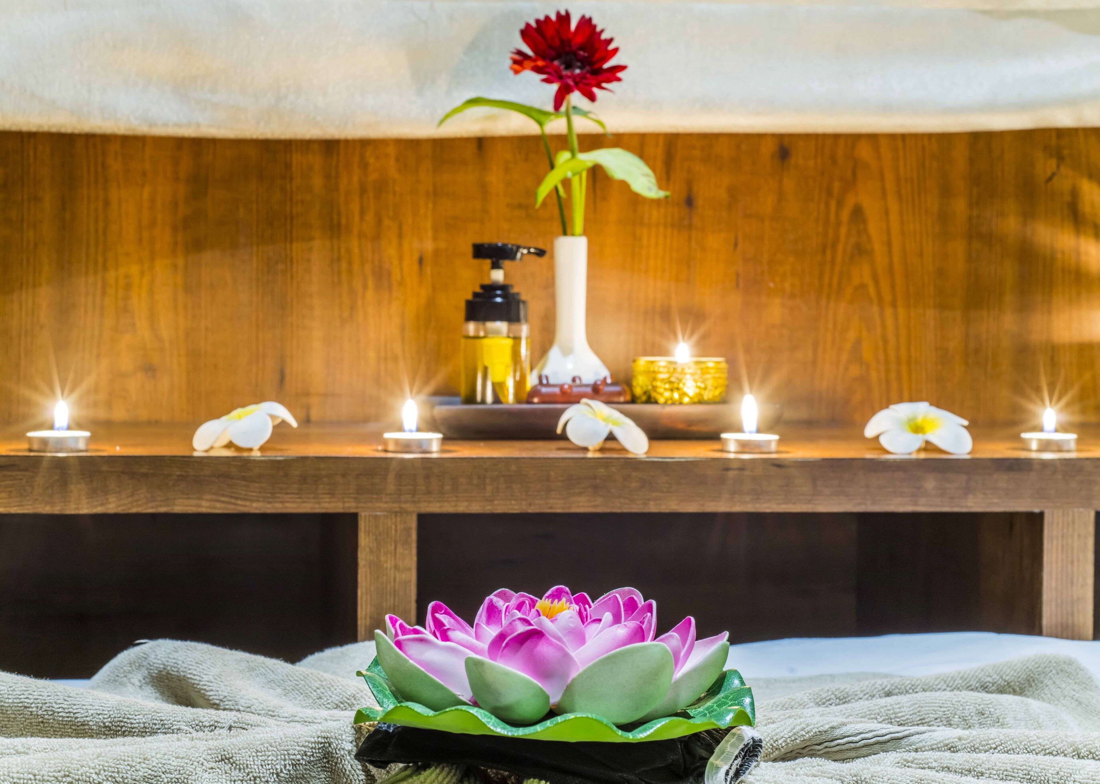 Uma mesa de madeira com velas, um vaso de flores e um arranjo de flores de lótus.