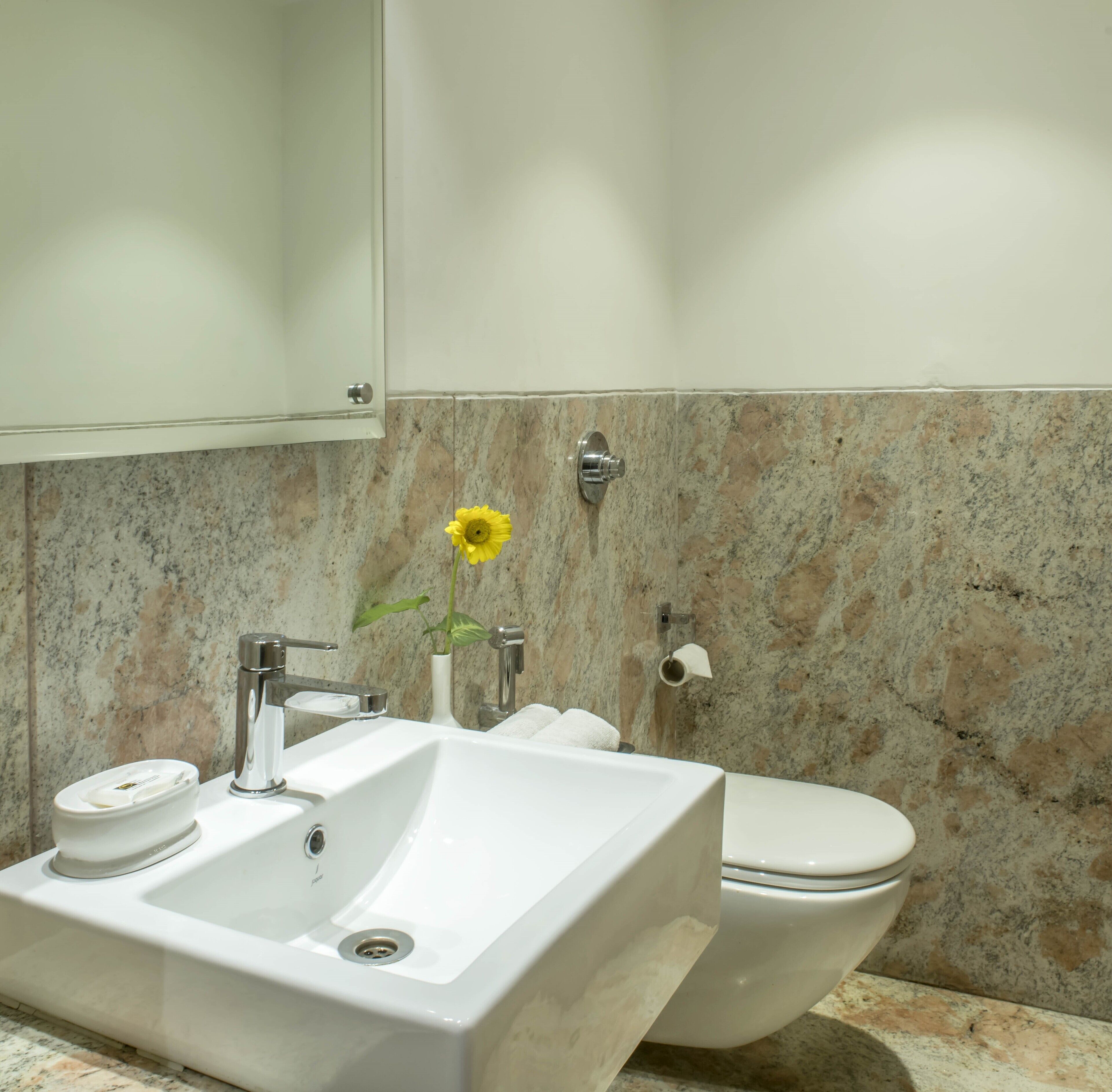 Un baño con un lavamanos blanco, un inodoro y una pared de mármol.