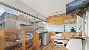 A modern kitchen with wooden cabinets, a built-in oven, and a dining area with two white chairs. - Heart Of The City Minutes From Macleay Street (Potts Point)