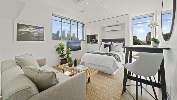 A modern bedroom with a large bed, a desk, and a view of the city skyline through the windows. - Modern Potts Point Studio (Potts Point)