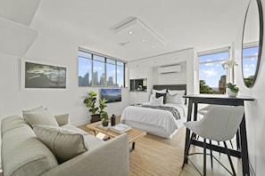 A modern bedroom with a large bed, a desk, and a view of the city skyline through the windows. - Modern Potts Point Studio (Potts Point)