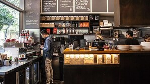 A coffee shop interior with a barista preparing drinks, shelves stocked with coffee beans, and a menu board. - Modern Potts Point Studio (Potts Point)