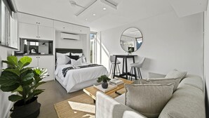 A modern hotel room with a bed, a seating area with a coffee table, a small table with chairs, a large mirror, and a potted plant. - Modern Potts Point Studio (Potts Point)