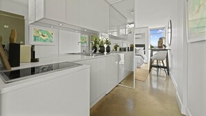 A modern kitchen with white cabinetry, a built-in island, and a dining area with a bar stool. - Modern Potts Point Studio (Potts Point)