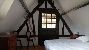 Un dormitorio con suelo de madera, una cama, un tocador, una silla y una ventana con vistas a zonas verdes.