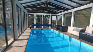 Una piscina interior con techo de vidrio, suelo de baldosas y una zona de estar con cojines.