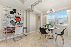 Un coin repas agrémenté d’une affiche de Mickey Mouse, d’un lustre et d’une fenêtre avec des stores.