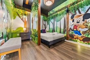 Une chambre d’enfant avec un lit, un banc et une fresque représentant Mickey Mouse.