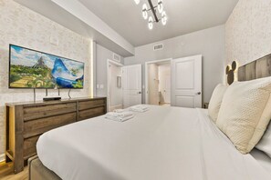 A hotel room with a large bed, a flat-screen TV mounted on the wall, and a wooden dresser.