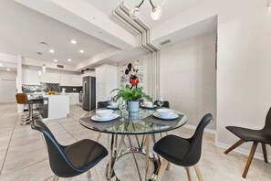 A modern kitchen with white cabinets, a central island, and a dining area with a glass table and black chairs.