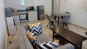 A compact living space with a kitchenette, a sofa with patterned cushions, a glass dining table, and a small coffee table. - Inviting 1-bed Apartment in Malindi (Malindi)