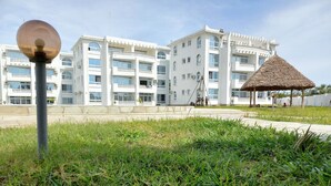 A building with multiple floors and balconies, a grassy area in the foreground, and a thatched-roof structure in the background. - Inviting 1-bed Apartment in Malindi (Malindi)