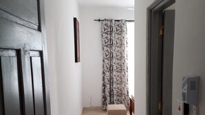 A hallway with a door on the left, a patterned curtain on the right, a small stool, and a tiled floor. - Kijani Homes Apartments Ocean Beach Drive (Malindi)