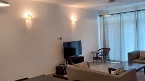 A living room with a dining table, sofa, TV, and ceiling fan. - Kijani Homes Apartments Ocean Beach Drive (Malindi)