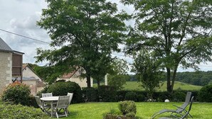 Een gazon met een tafel en stoelen, een kleine tuin en een gebouw op de achtergrond.