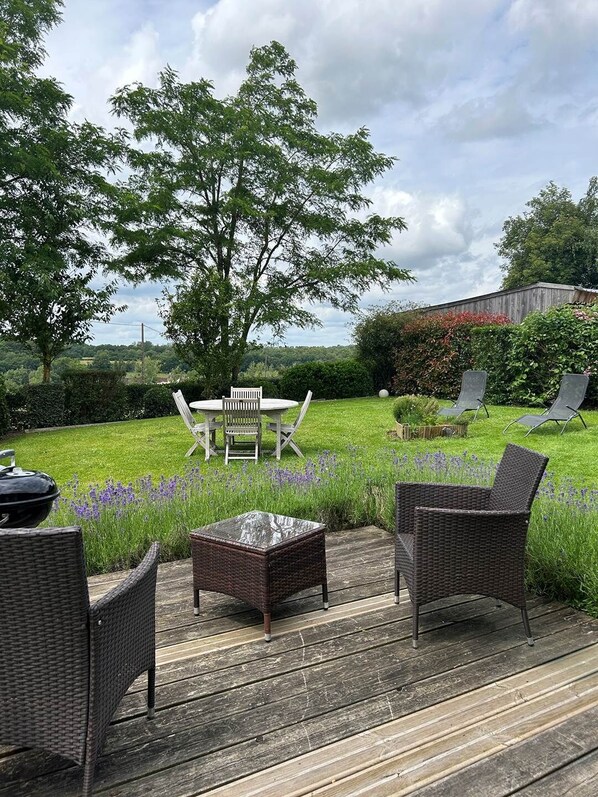 Une terrasse dotée de meubles en osier, d’une table avec des chaises et d’un espace gazonné agrémenté de fleurs.