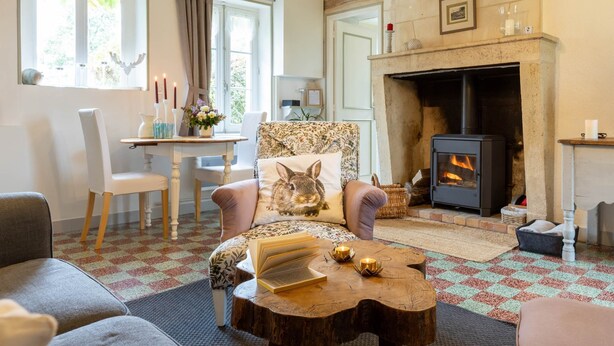 Een gezellige woonkamer met een open haard, een comfortabele bank, een houten salontafel en een eethoek met een tafel en stoelen.