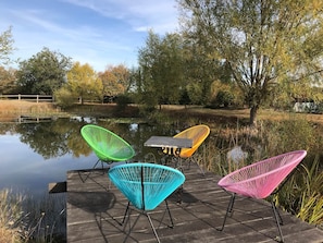 A wooden deck with four colorful chairs and a table by a calm pond. - La Petite Maison - Nature and Calm (Fléré-la-Rivière)