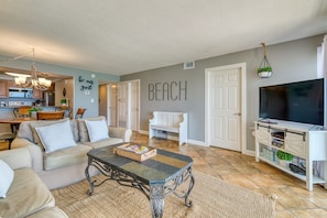 A living room with a sofa, coffee table, TV stand, and a wall with 'BEACH' written on it.