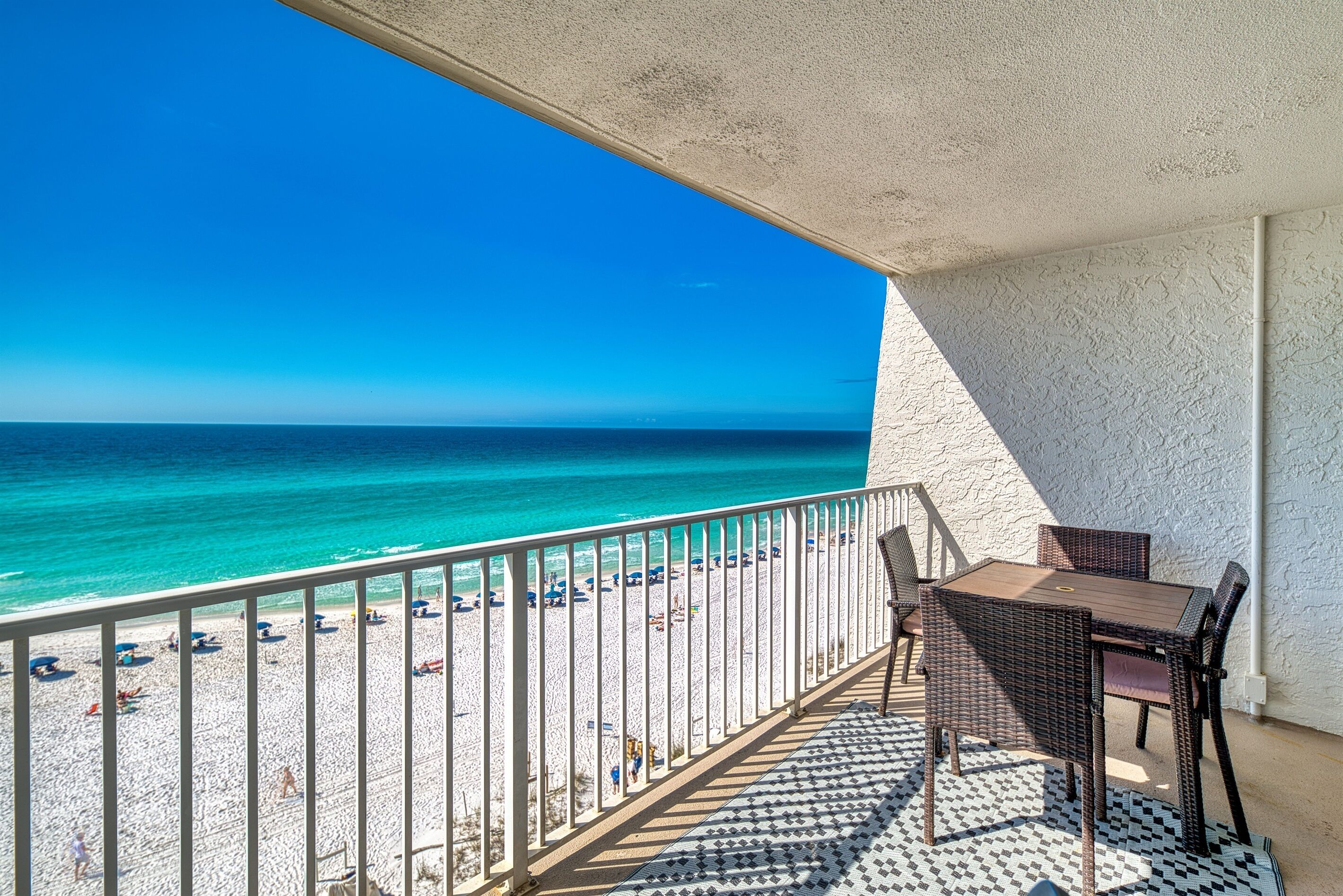 A balcony with a view of the beach and ocean, a table, and chairs.