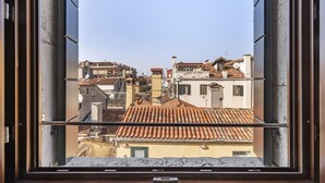 Une vue par la fenêtre sur un paysage urbain, avec des bâtiments dotés d’une architecture traditionnelle et de toits couverts de tuiles.