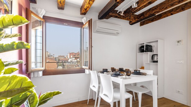 Un coin repas avec une table blanche, des chaises et une vue sur la ville, visible à travers une grande fenêtre.