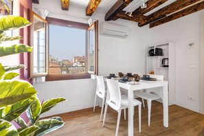 Un coin repas avec une table blanche, des chaises et une vue sur la ville, visible à travers une grande fenêtre.