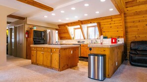 A kitchen with wooden cabinets, a stainless steel trash can, and a black leather chair. - Furnished Deck + Fire Pit: Happy Jack Cabin (Happy Jack)