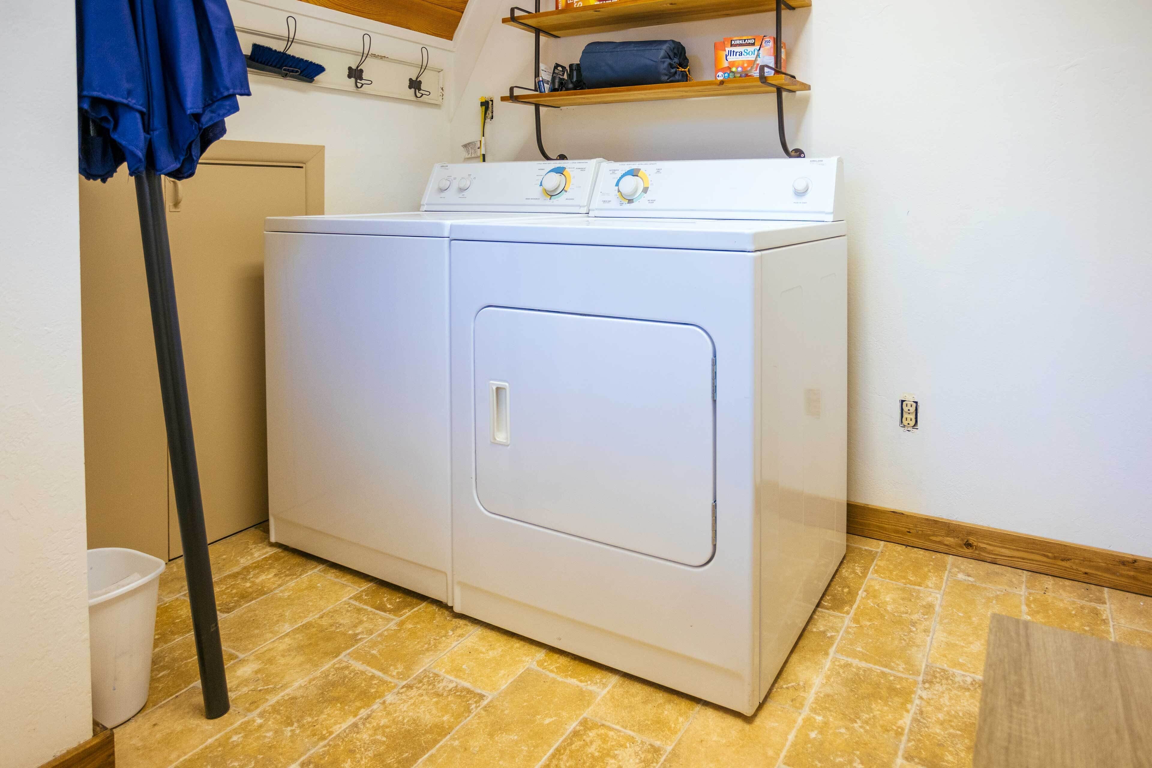 A laundry room with a front-loading washer and dryer, a broom, and a shelf with storage items.