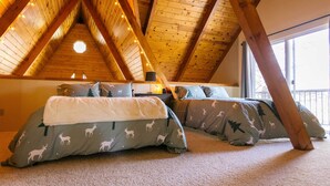 A cozy attic bedroom with wooden beams, two beds with deer-patterned bedding, and a large window. - Furnished Deck + Fire Pit: Happy Jack Cabin (Happy Jack)