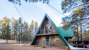 A cabin with a triangular roof, a balcony, and a stone foundation. - Furnished Deck + Fire Pit: Happy Jack Cabin (Happy Jack)