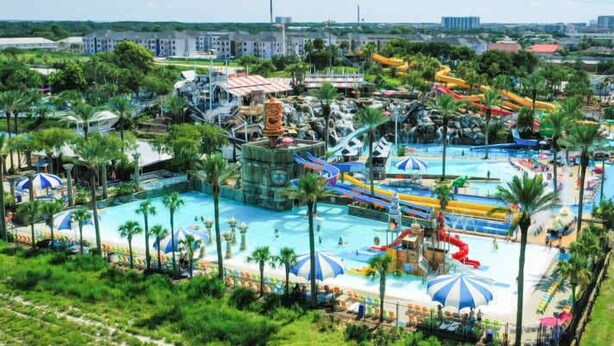Parque acuático con múltiples toboganes y piscinas, rodeado de palmeras y sombrillas.