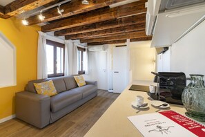 Un salón moderno con un sofá, una cafetera y un florero de vidrio sobre una mesa.