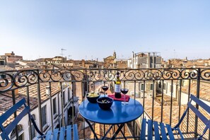 A balcony with a table set for two, overlooking a cityscape with terracotta rooftops.