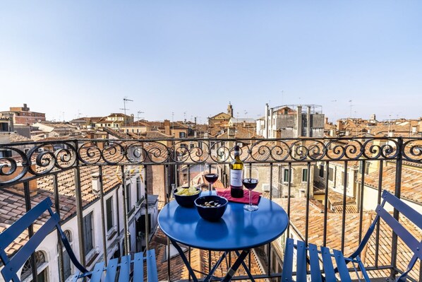 Un balcón con una mesa dispuesta para dos personas, con vista a un paisaje urbano de tejados de terracota.