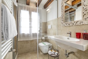 A bathroom with a glass shower enclosure, a white sink, and a mirror with an ornate frame.