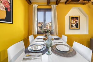Una mesa de comedor dispuesta con platos, vasos y cubiertos, con una ventana y cortinas al fondo.