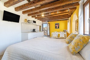 Un dormitorio con cama, televisor en la pared, zona de cocina y mesa de comedor con sillas.