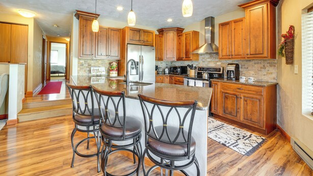 A kitchen with wooden cabinets, a stainless steel refrigerator, a built-in island with bar stools, and a stone backsplash. - Idyllic Somerset Condo: Ski, Hike & Relax! (Somerset)