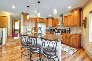 A kitchen with wooden cabinets, a stainless steel refrigerator, a built-in island with bar stools, and a stone backsplash. - Idyllic Somerset Condo: Ski, Hike & Relax! (Somerset)