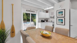 Une cuisine moderne avec des meubles blancs, un coin repas doté d’une table en bois et une vue sur le jardin extérieur.