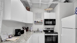 Une cuisine compacte avec des meubles blancs, un four à micro-ondes, une cuisinière et un réfrigérateur.